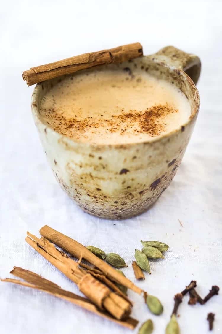 یک فنجان چای ماسالا در کنار ادویه های دارچین، هل سبز و میخک